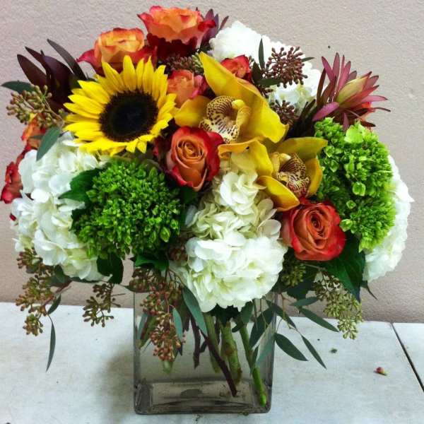 Mixed bouquet with sunflowers, roses, orchids, and white hydrangeas in a glass vase