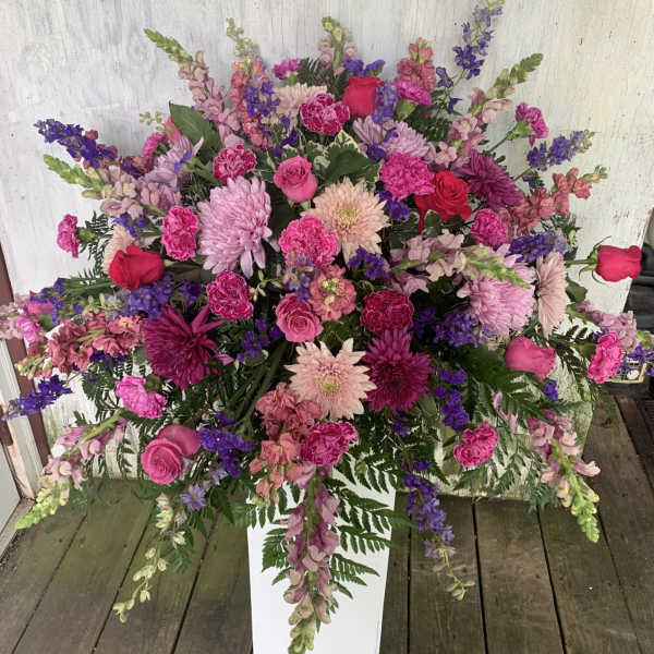 Large pink and purple floral arrangement in a white pedestal vase