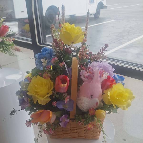 Colorful basket of mixed flowers with yellow roses, tulips, and a pink plush bunny toy