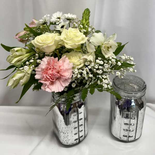 Pink and white flowers arranged in a mirrored jar vase beside an empty jar.