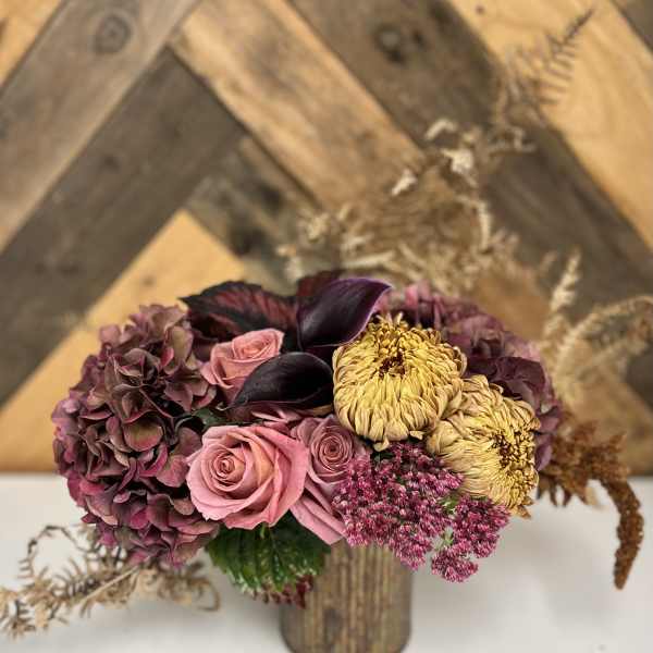 Bouquet of pink roses, purple hydrangea, and yellow chrysanthemums in a wooden vase