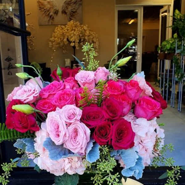 Low round arrangement of hot pink and light pink roses in a glass vase on a clear stand
