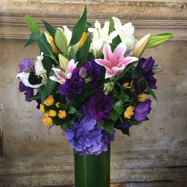 Mixed bouquet of lilies, roses, and hydrangeas in a tall green vase