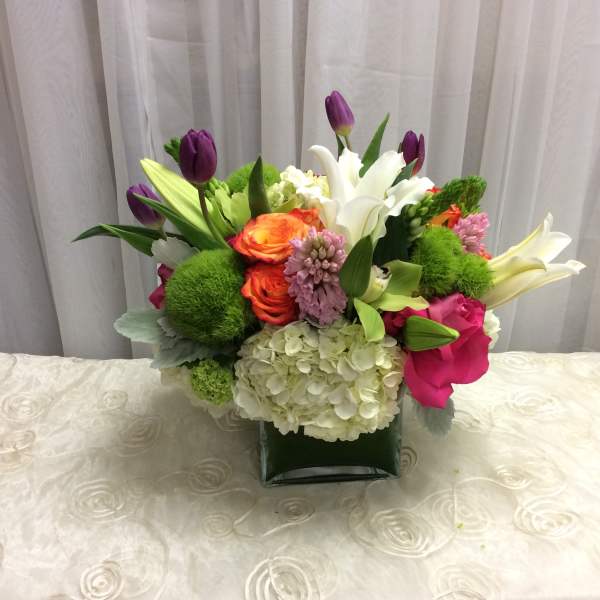 Mixed bouquet with lilies, tulips, roses, and hydrangea in a square vase