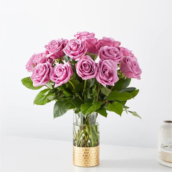 Arrangement of lavender-pink roses in a clear glass vase with a gold metal base