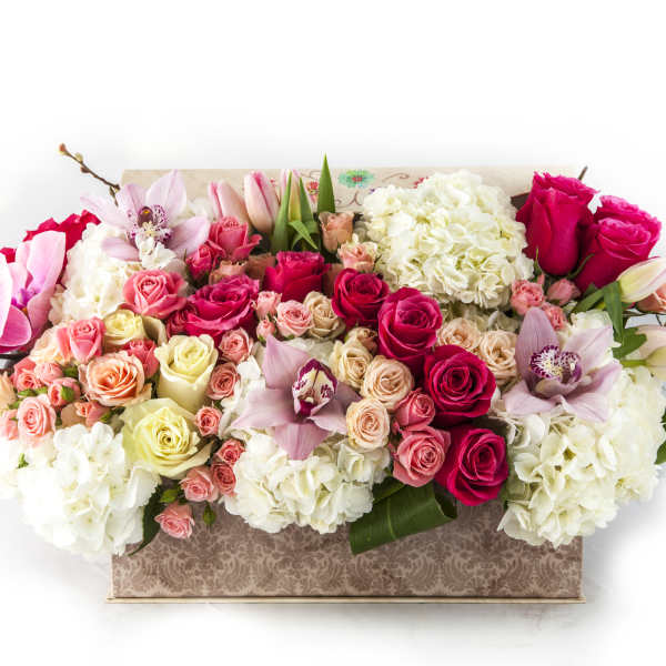 Mixed bouquet of pink roses, orchids, and white hydrangeas in a patterned box