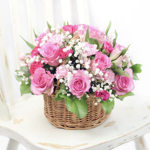 Round basket of pink roses and carnations with white filler flowers.