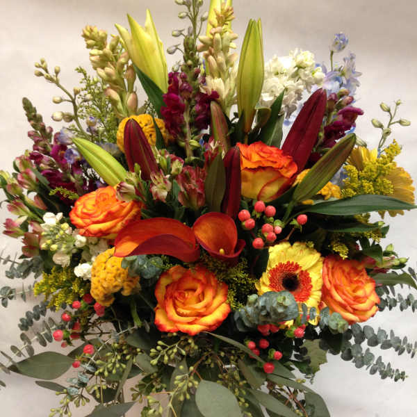Mixed bouquet of orange roses, lilies, and calla lilies in a glass vase