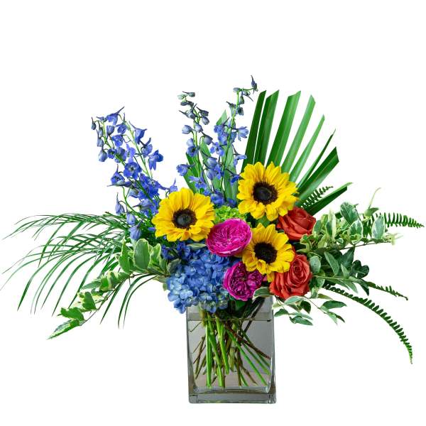 Bright mixed bouquet in a square glass vase with sunflowers, blue flowers, and roses