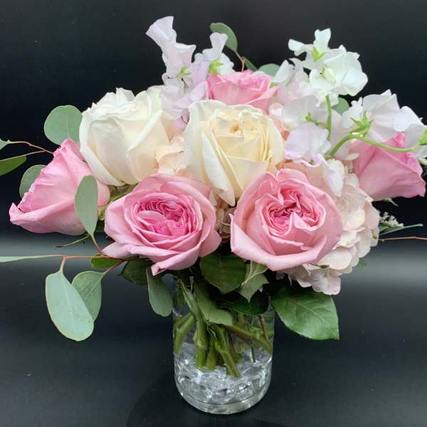 Compact arrangement of pink and cream roses with soft blush blooms in a clear glass vase.