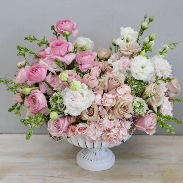 Low compote arrangement of pink and blush roses, hydrangeas, and white lisianthus in a white pedestal bowl