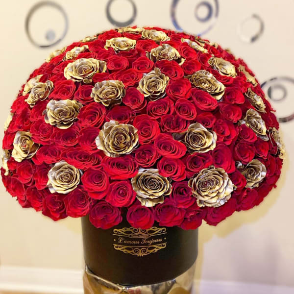 Large dome of red and gold roses arranged in a black hat box on a metallic pedestal