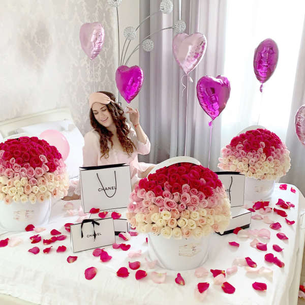 Large hatbox arrangements of pink and white roses on a bed with heart balloons and gift bags.