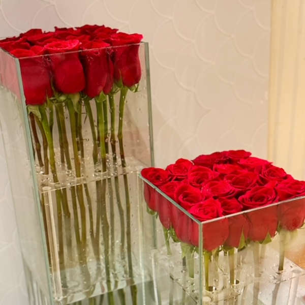Two clear glass vases filled with tightly packed red roses.