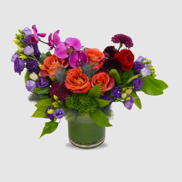 Colorful bouquet of roses, orchids, and purple blooms in a glass vase