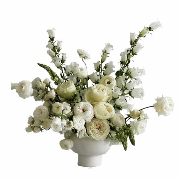 Low white compote arrangement of ivory roses and ranunculus with airy white accent flowers
