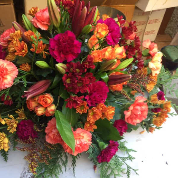 Low mound of orange and red flowers with lilies, roses, carnations, and mums in a spray-style arrangement.