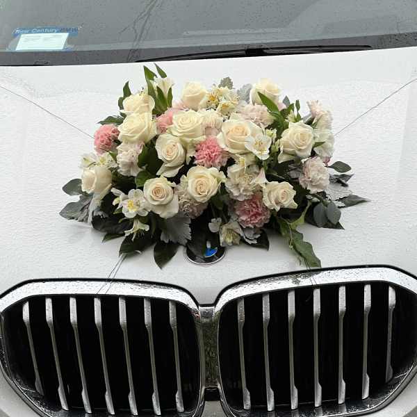 Cream and pink floral arrangement mounted on the hood of a white BMW.