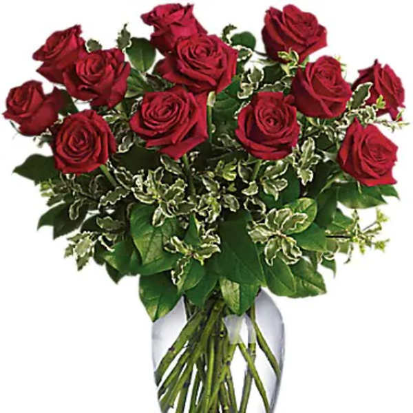 Arrangement of red roses in a clear glass vase with variegated foliage
