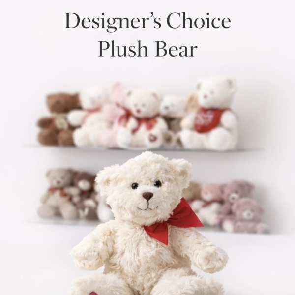 Cream plush teddy bear with red bow and heart on paw, with other teddy bears blurred in the background