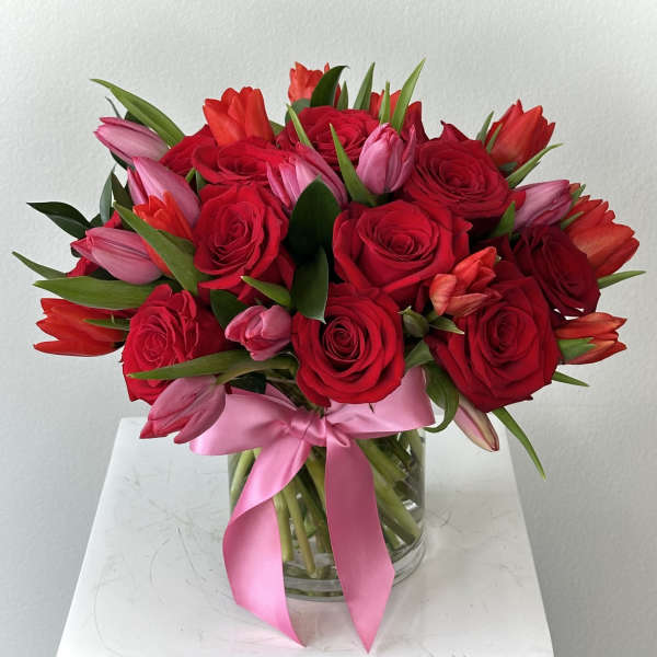 Bouquet of red roses and pink tulips in a glass vase with a pink ribbon