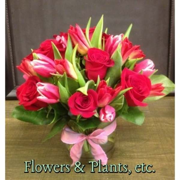 Bouquet of red roses and pink tulips in a glass vase with a pink ribbon