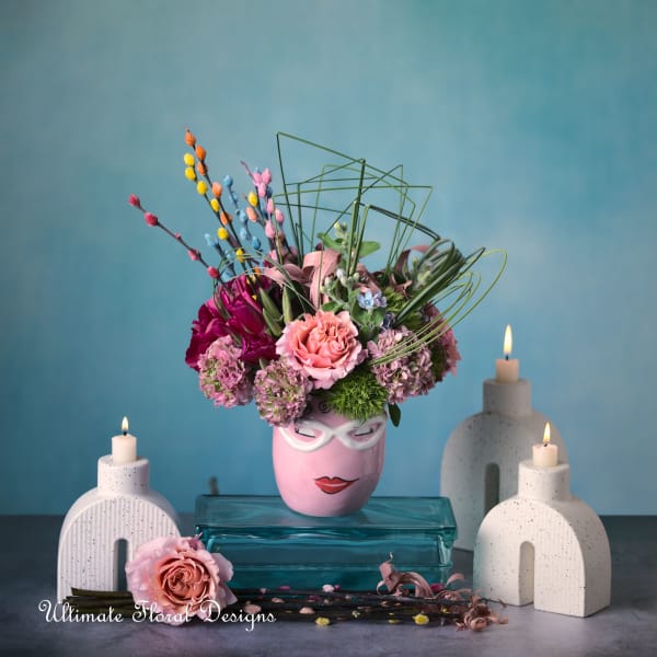 Pink floral arrangement in a painted face vase with candles around it