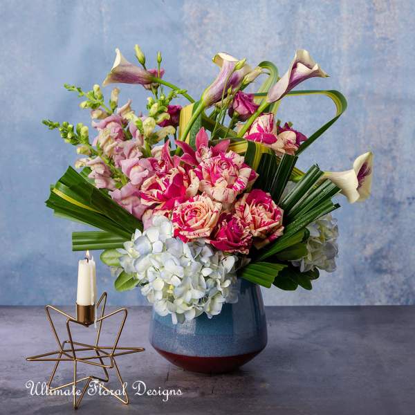 Mixed bouquet of pink roses, calla lilies, and hydrangeas in a blue vase