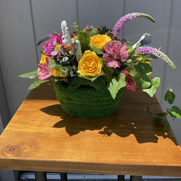 Low basket arrangement with yellow roses, pink blooms, and trailing ivy in a green textured container
