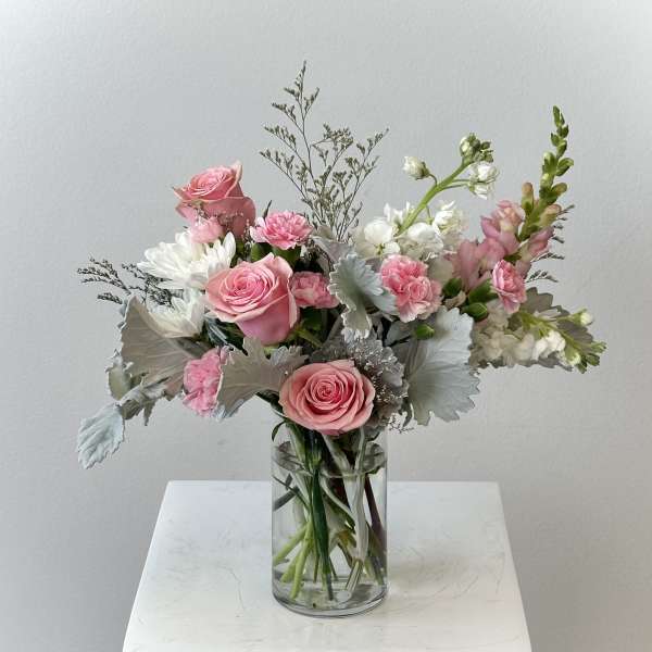 Pink and white flower arrangement with roses and carnations in a clear glass vase