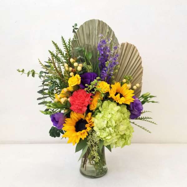 Mixed bouquet in a glass vase with sunflowers, hydrangea, and purple blooms