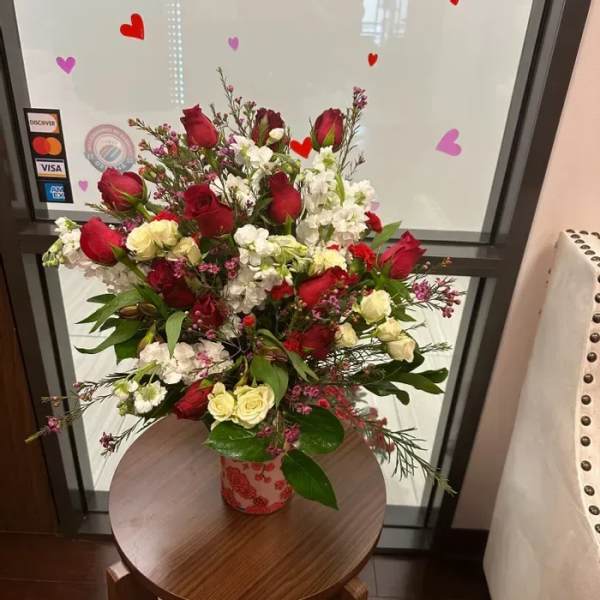 Tall arrangement of red roses, white flowers, and cream spray roses in a patterned ceramic vase