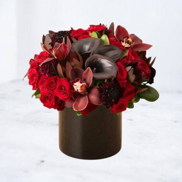 Low red rose and dark calla lily arrangement with orchids in a round black vase