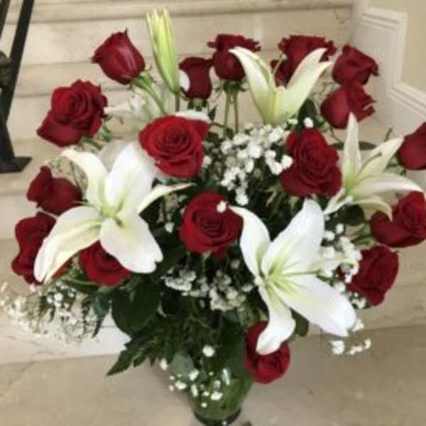 Tall arrangement of red roses and white lilies in a clear glass vase