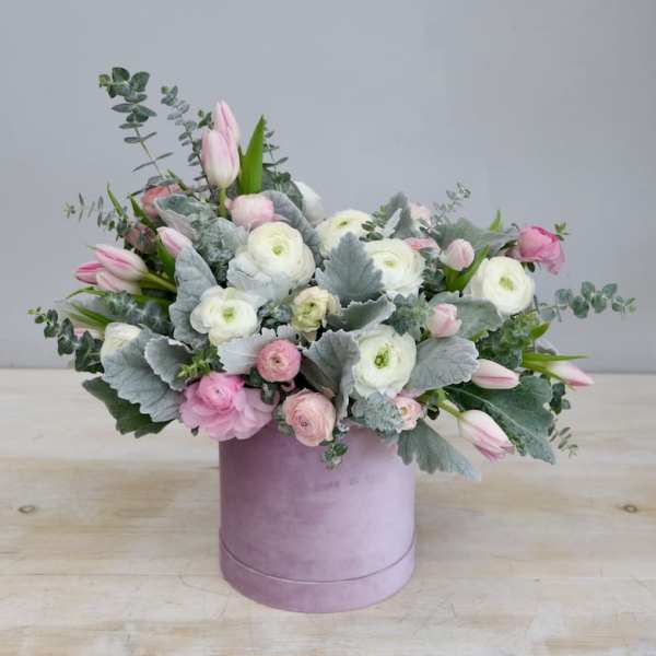 Pastel pink and white flower arrangement with silver foliage in a round lavender hatbox.
