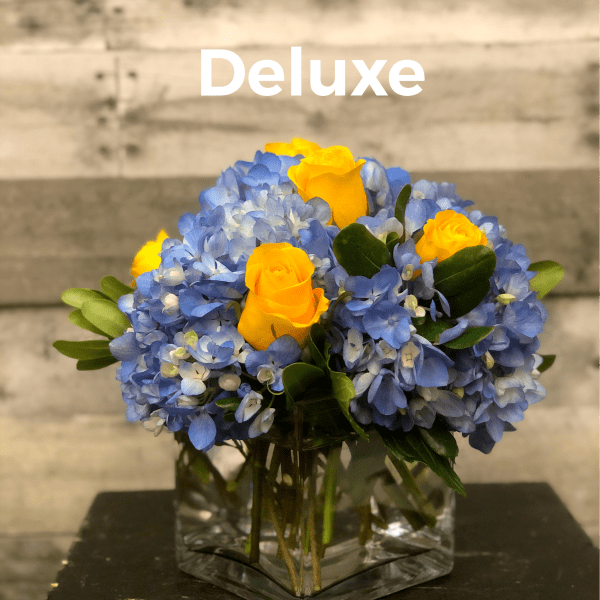 Blue hydrangeas and yellow roses in a clear square vase