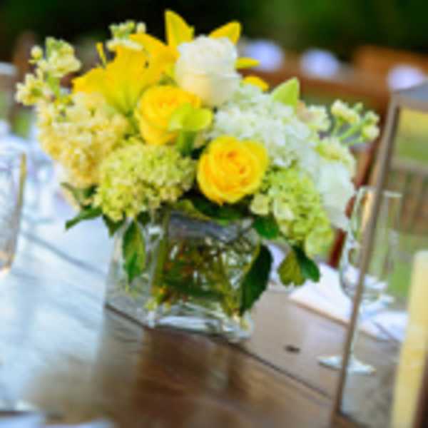 Yellow lilies and roses with white blooms in a clear cube vase on a table