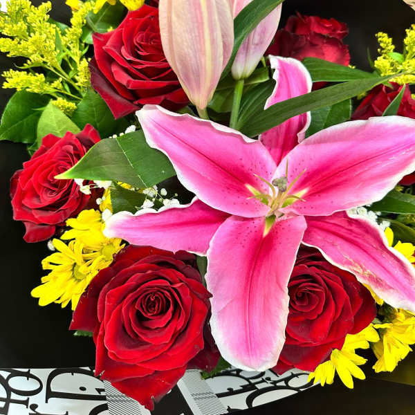 Bouquet of pink lilies, red roses, and yellow daisies wrapped in black and white paper