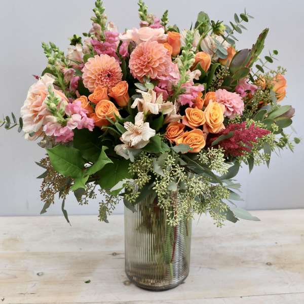 Tall mixed bouquet of pink and orange flowers in a ribbed glass vase