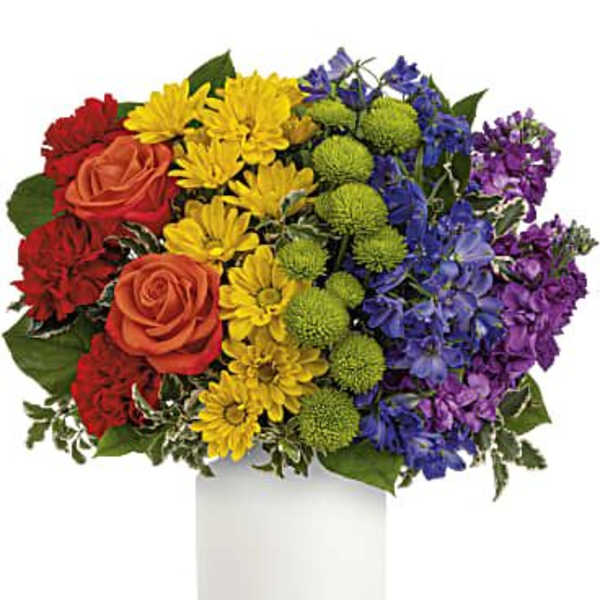Rainbow bouquet of roses, daisies, and purple flowers in a white vase