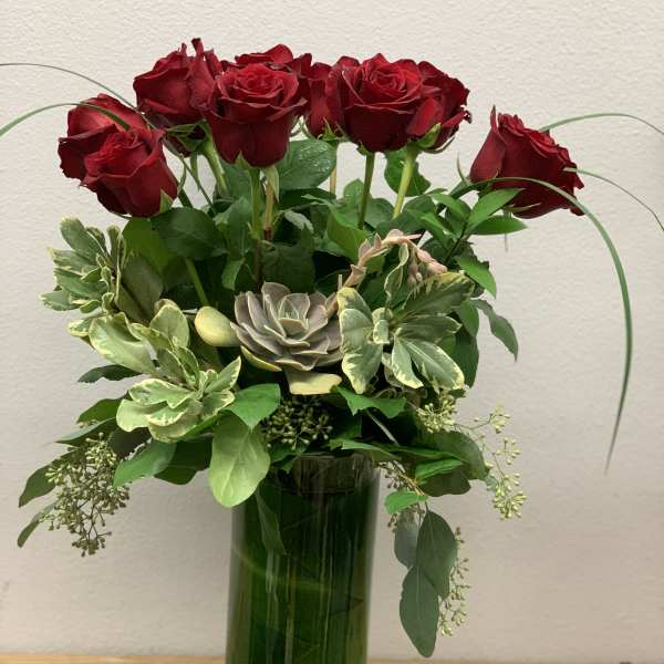 Red roses and succulents arranged in a tall green glass vase