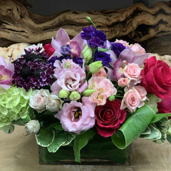 Mixed bouquet of roses, orchids, and hydrangeas in a low glass vase