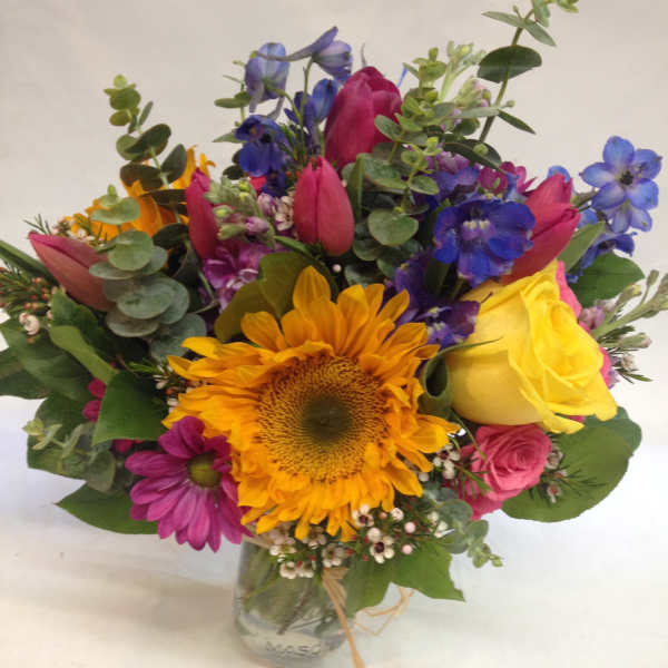 Mixed bouquet with sunflowers, roses, and blue flowers in a glass vase