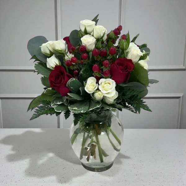 Arrangement of red and white roses with red berries in a round clear glass vase.