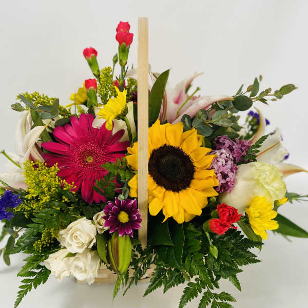 Mixed bouquet with sunflowers, gerbera daisies, roses, and carnations in a wooden basket