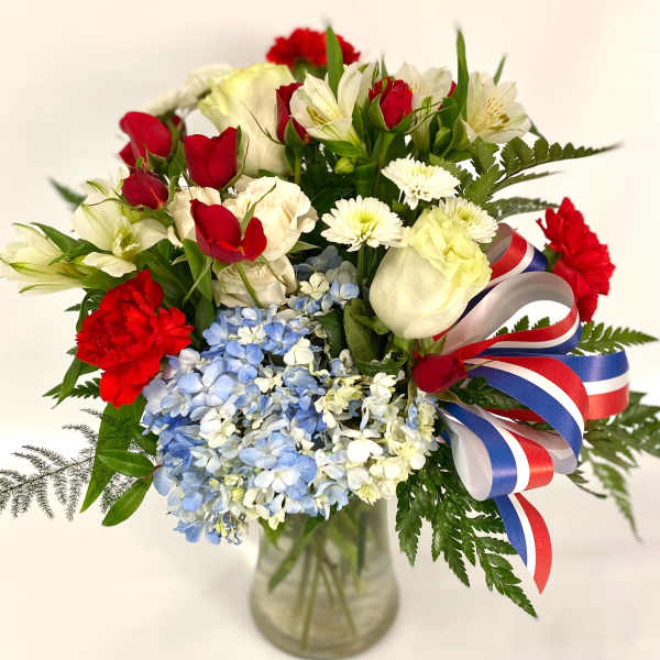 Bouquet of red and white flowers with blue hydrangeas in a glass vase