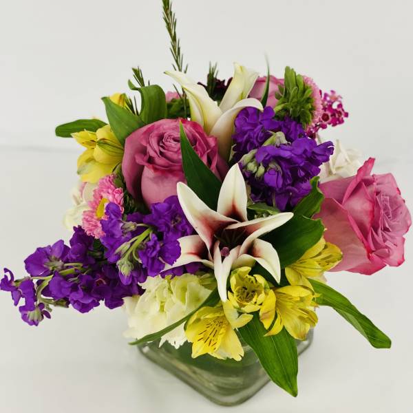 Mixed bouquet with pink roses, white lilies, and purple flowers in a glass vase