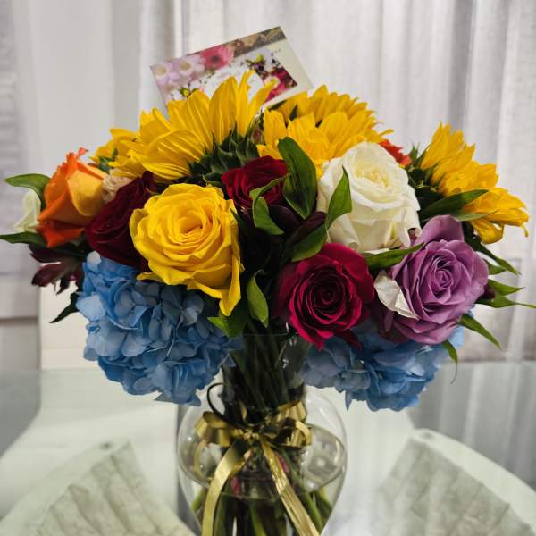 Colorful bouquet of roses, sunflowers, and hydrangeas in a glass vase