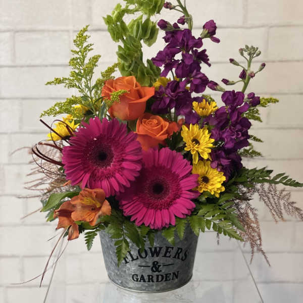 Mixed bouquet in a metal bucket with pink gerberas, orange roses, and purple blooms