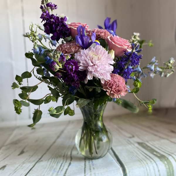 Mixed pink, purple, and blue flowers arranged in a clear glass vase.